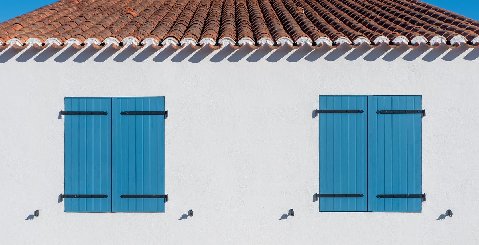 Façana blanca amb finestrons blaus i teulada de teula